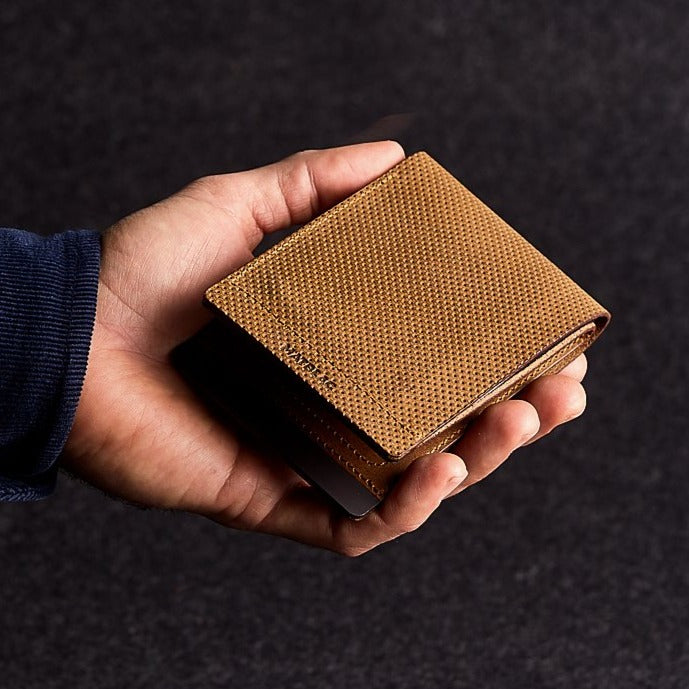 Close up of man holding a minimalist brown genuine leather magnetic wallet on grey background