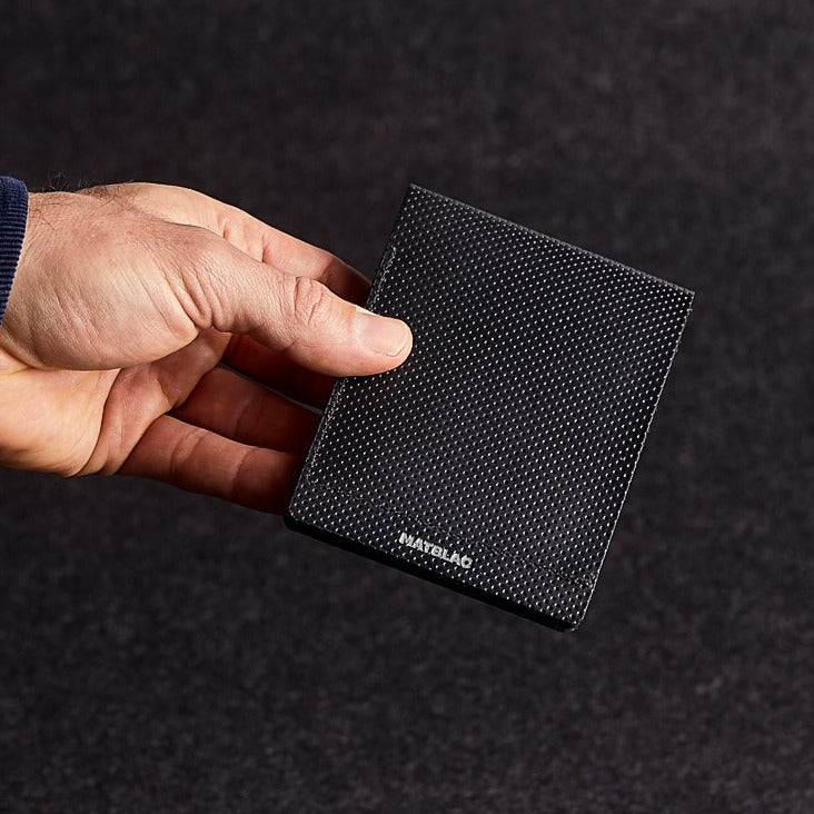 A man's hand holding a minimalist black genuine leather wallet on a grey felt background