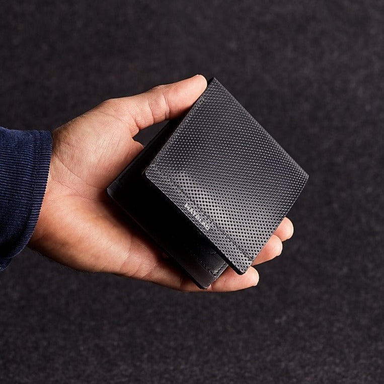 A man's hand holding a minimalist black genuine leather wallet on a grey felt background