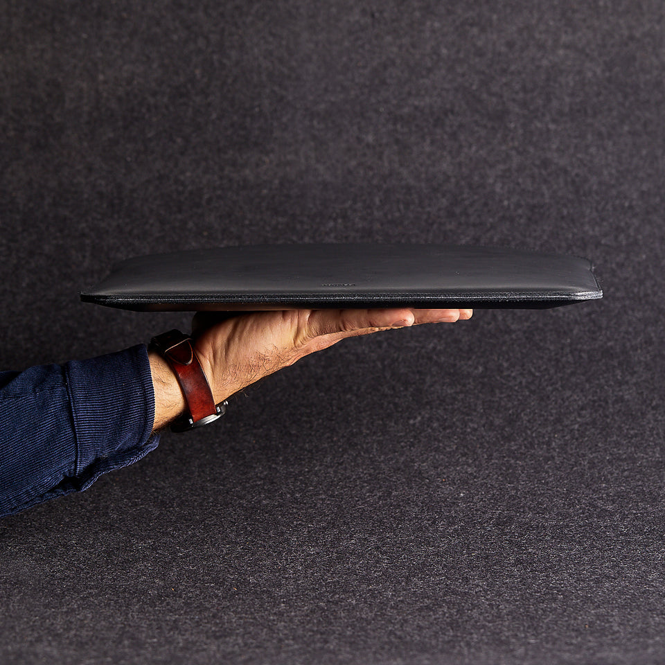 Side view of minimalist black genuine leather laptop bag held by a man's arm