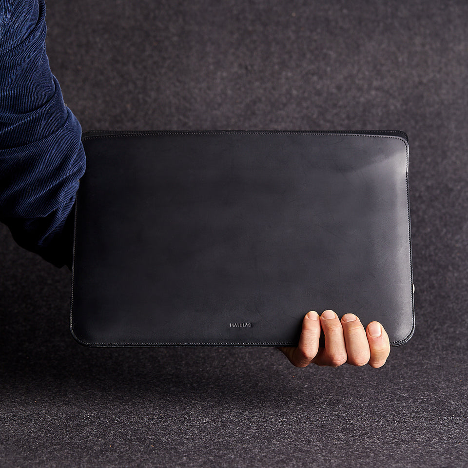 Close up of minimalist black genuine leather laptop bag held by a man's arm