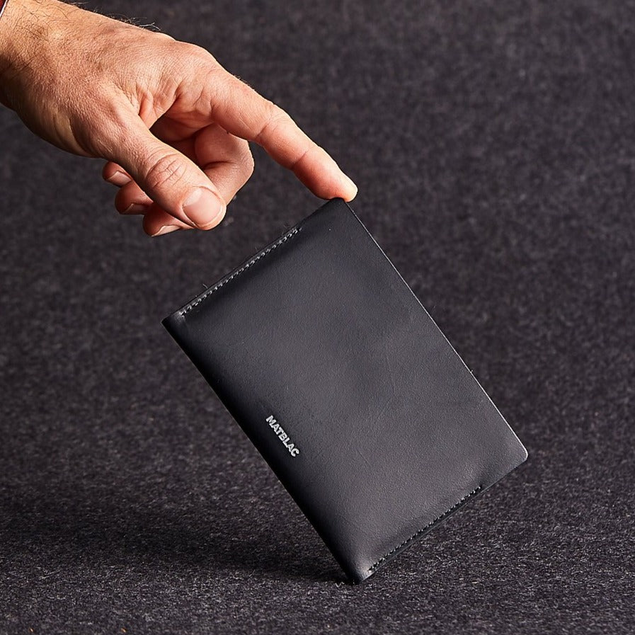 Man's finger balancing black genuine leather passbook on grey felt background