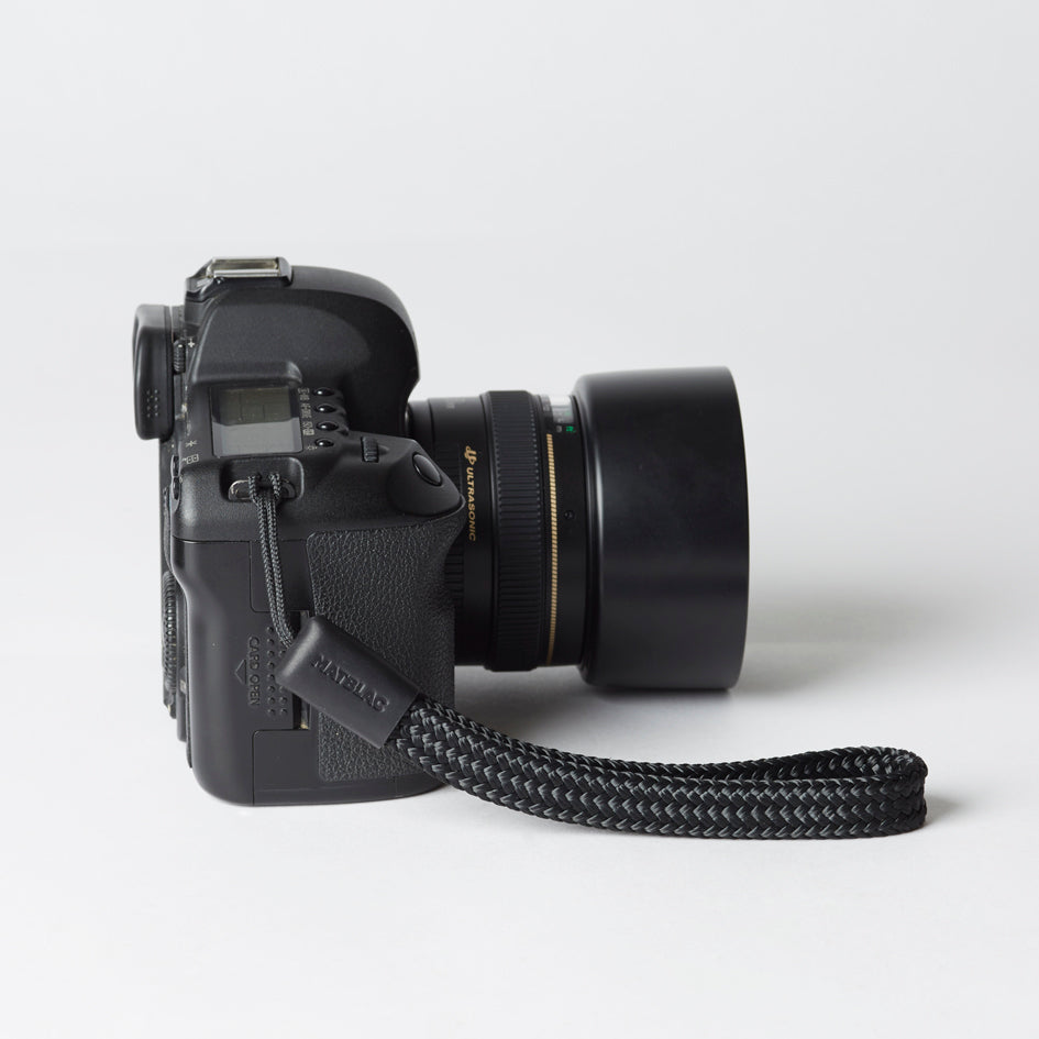 Black minimalist camera wrist strap with leather ends connected to a camera