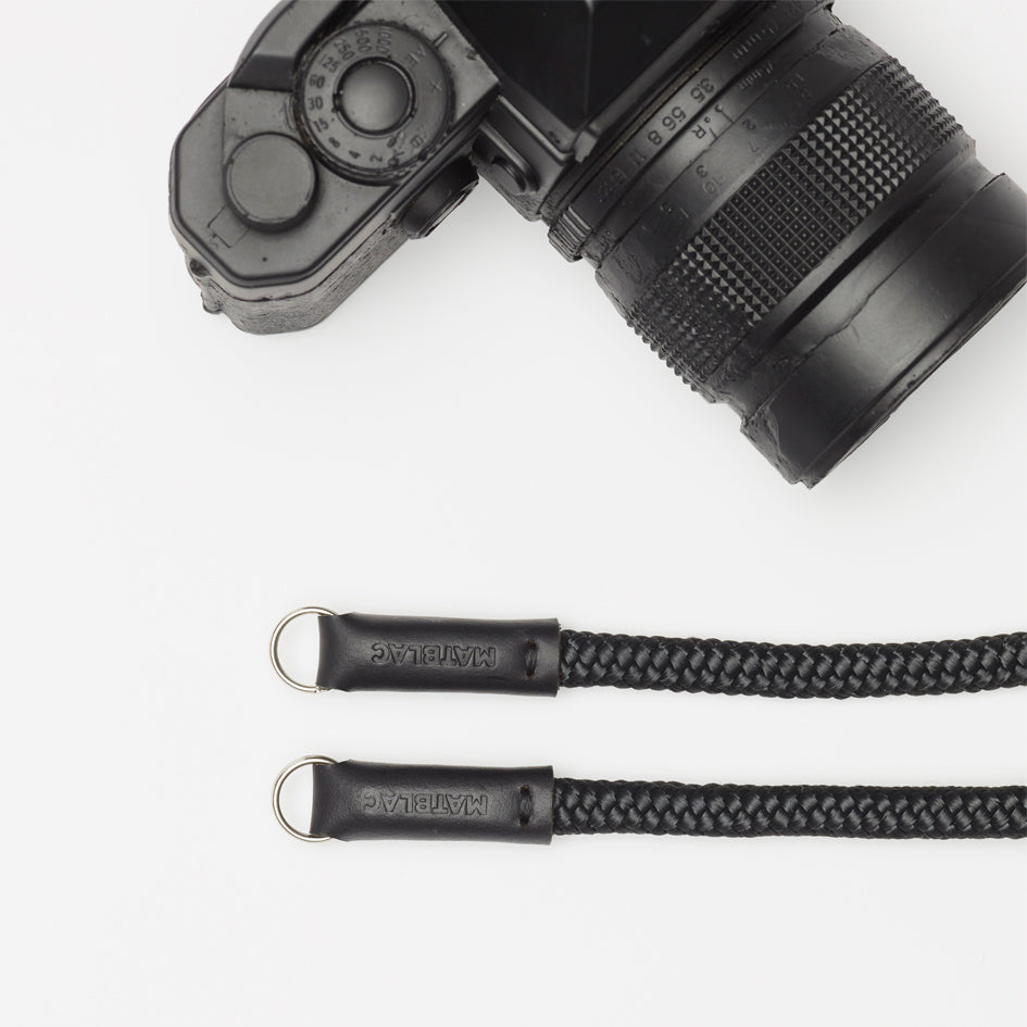 ends of a black camera strap and black camera on white background