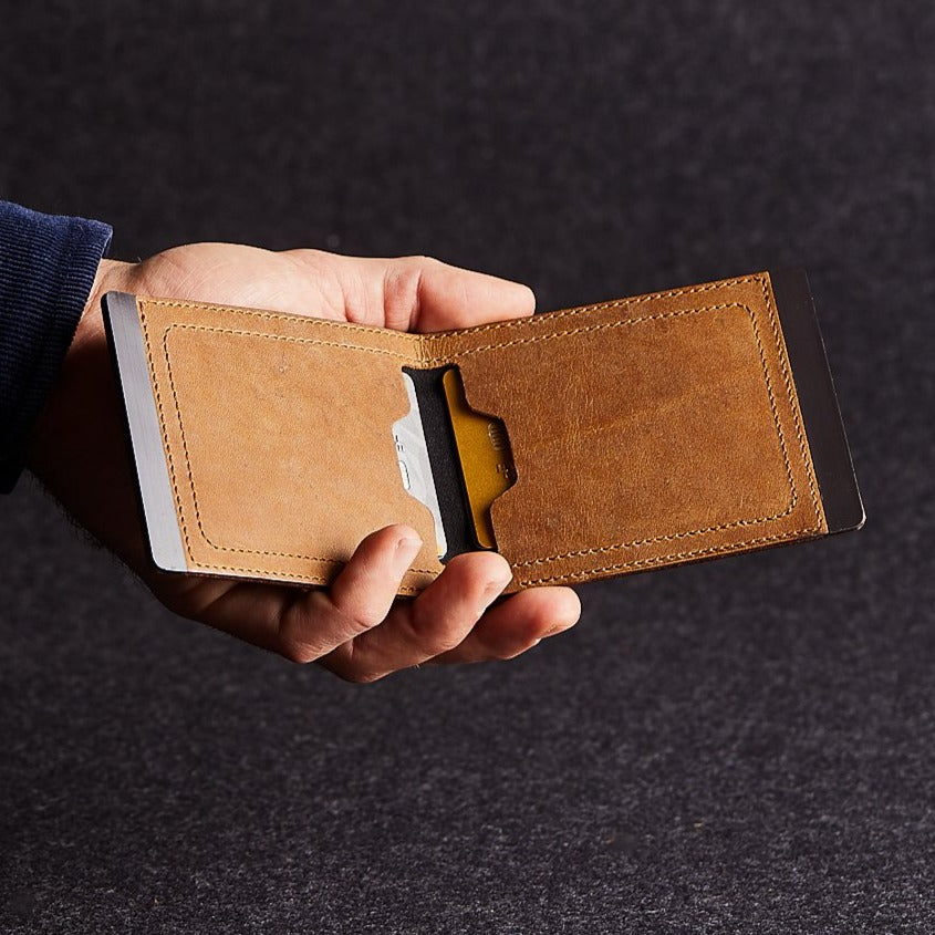 Close up of man holding a minimalist brown genuine leather magnetic wallet on grey background