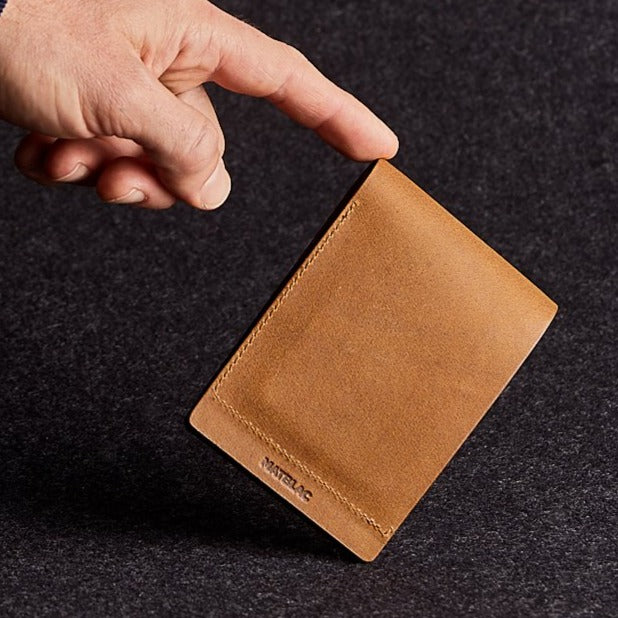 Close up of man's finger balancing a minimalist brown genuine leather magnetic wallet