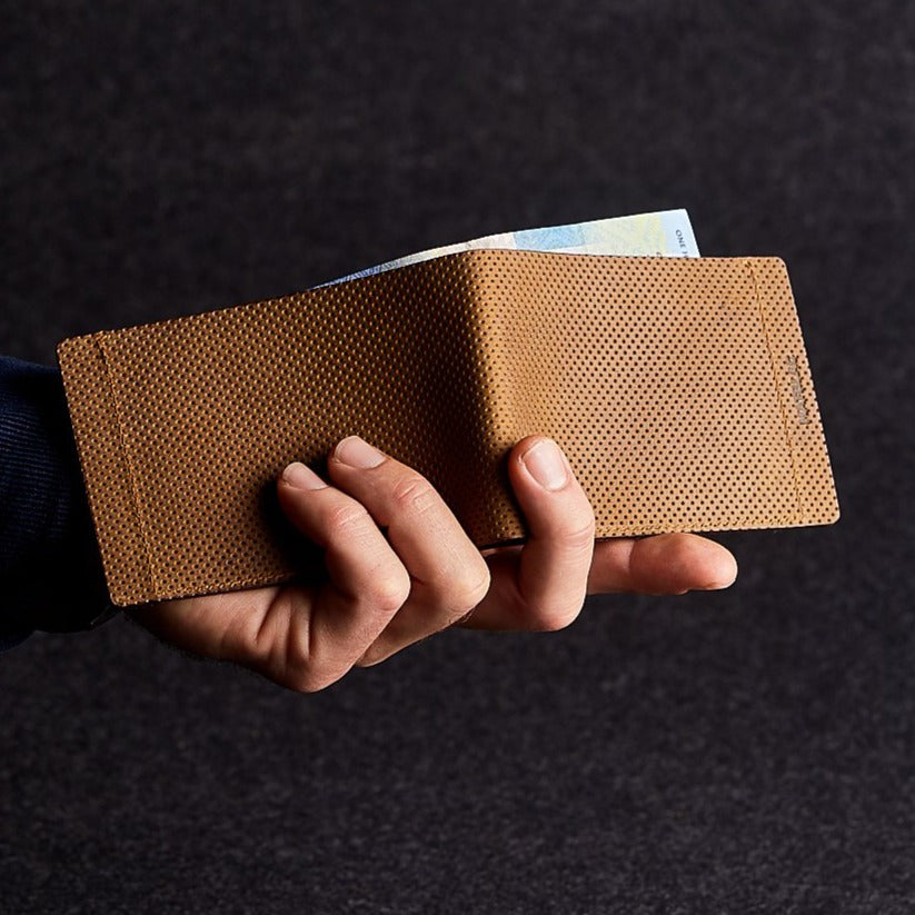 Close up of man holding a minimalist brown genuine leather magnetic wallet open on grey background