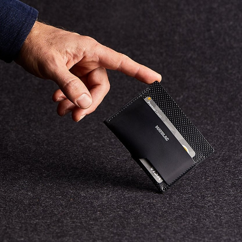 Man's finger balancing a black genuine leather cash slip wallet on grey felt background.