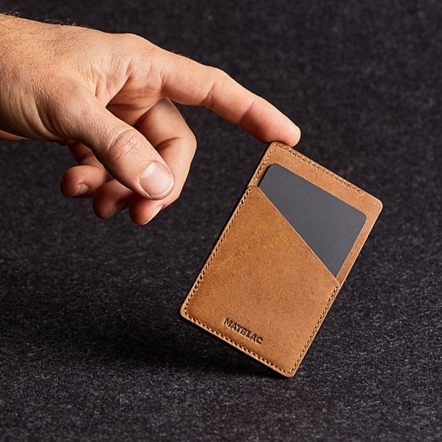 Man's finger balancing a brown genuine leather quickdraw slim wallet on grey background