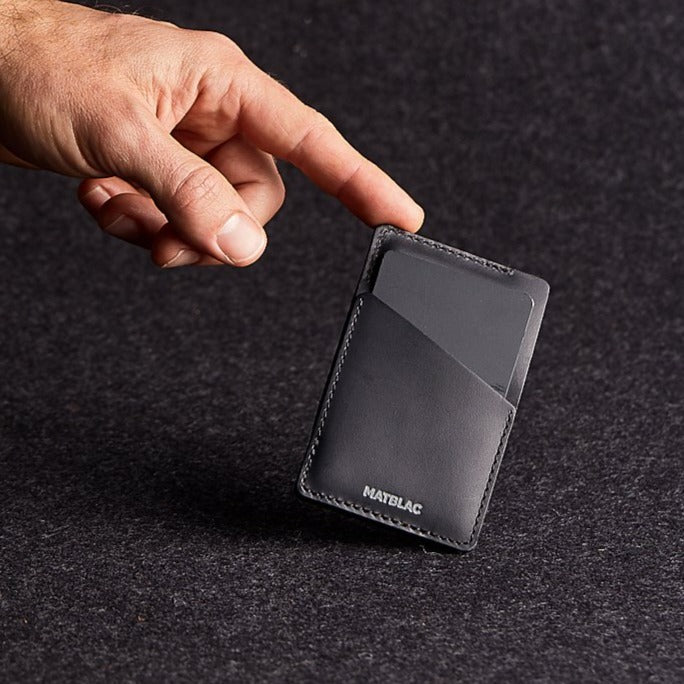 Man's finger balancing black genuine leather quickdraw slim wallet on grey felt background