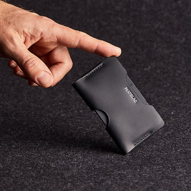 Close up of man balancing black genuine leather micro wallet on grey felt background