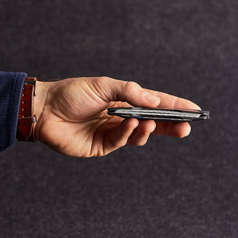Close up of man holding black genuine leather micro wallet on grey felt background