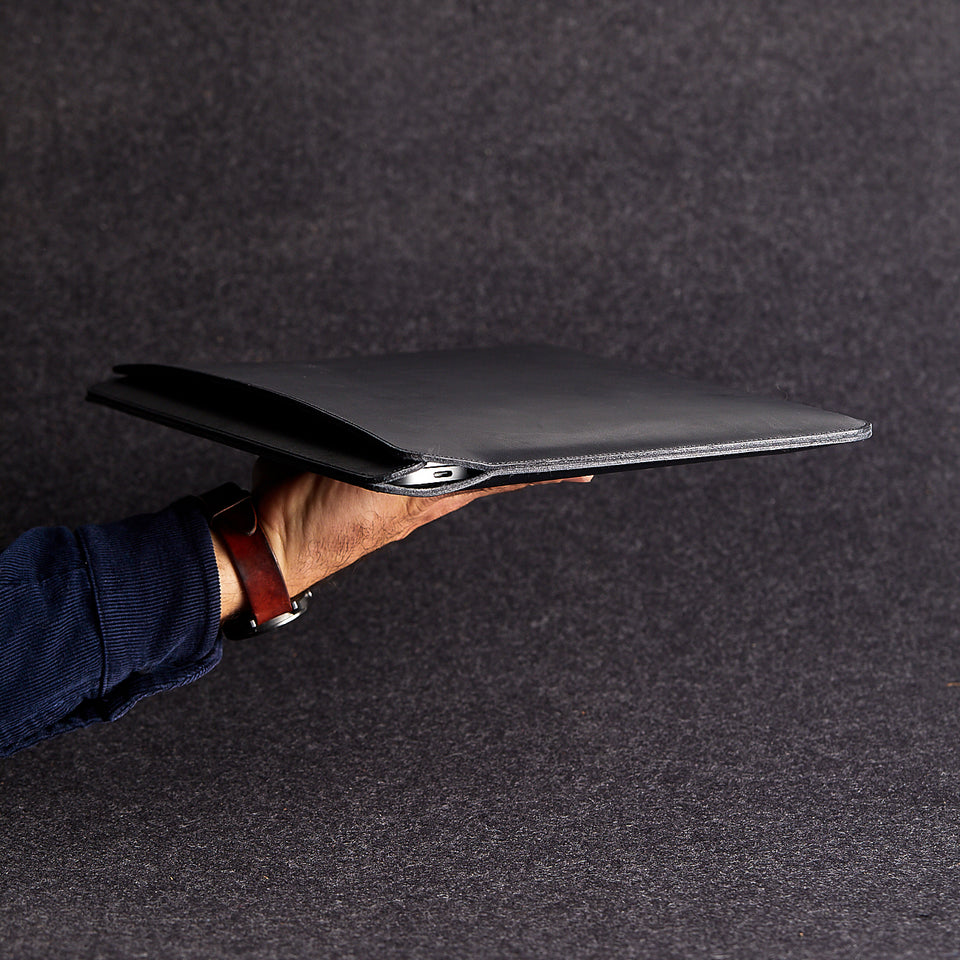 Side view of minimalist black genuine leather laptop bag held by a man's arm
