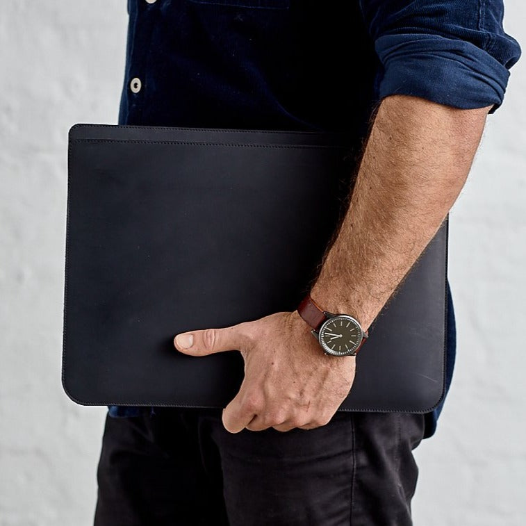 Man holding minimalist black genuine leather laptop bag against white background